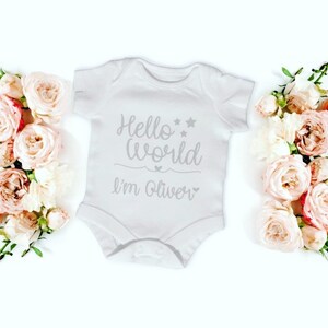 May include: White baby onesie with the text "Hello World I'm Oliver" in grey lettering with two stars and two hearts.