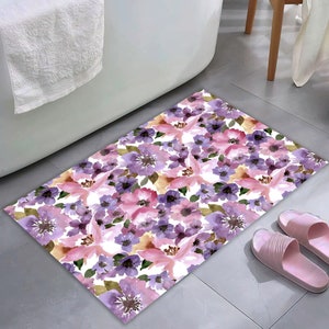 May include: A white bath mat with a floral pattern featuring pink and purple flowers. The flowers are painted in a watercolor style.