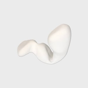 May include: White ceramic sculpture of an abstract shape resembling a curled up figure.