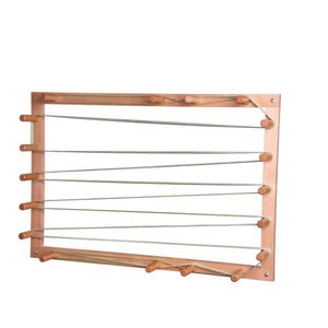 May include: A rectangular wooden weaving loom frame featuring a series of light-colored wooden pegs arranged along the perimeter. Thin, light-colored string is threaded back and forth between the pegs, creating a geometric pattern across the center.
