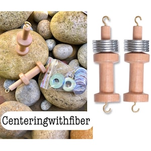 May include: Wooden spindle spinning tools with metal washers and hooks. The image also shows a bag of colorful rings and the text "Centeringwithfiber". The tools are light brown and the rings are various shades of blue and green.