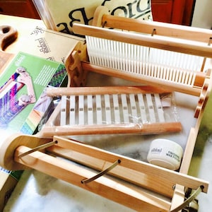 May include: A collection of wooden weaving tools and accessories, including a loom, a brush, and a jar of finishing wax polish. A canvas carry bag and printed materials are also visible. The text "Centeringwithfiber" is displayed at the bottom.
