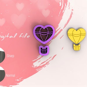 May include: Two heart-shaped hot air balloon cookie cutters, one purple and one yellow. The purple cutter has a basket with a heart shape. The cutters are on a pink background with hearts.