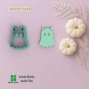 May include: Two teal-colored cookie cutters in the shape of ghosts, one with a bow and the other with horns. The phrase "DIGITAL FILES" is at the top. Two small white pumpkins and decorative sprigs are also in the image. The words "Include Bambu studio Files" are at the bottom.