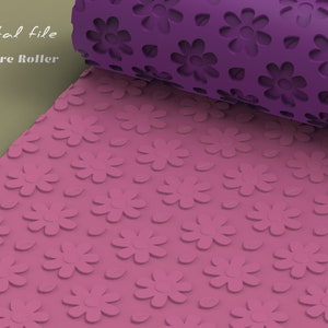 Può includere: Un rullo per texture rosa e viola con un motivo floreale. Il rullo è srotolato, rivelando una superficie rosa con fiori e foglie in rilievo. La parte arrotolata è viola con forme di fiori ritagliate. Le parole "Digital file" e "Texture Roller" sono visibili.