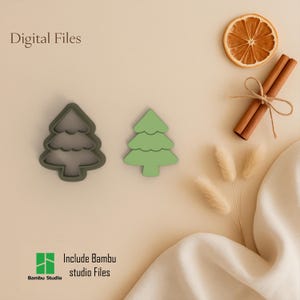 Può includere: Due formine per biscotti a forma di albero di Natale, una con un contorno grigio scuro e l'altra verde chiaro pieno. L'immagine include anche una fetta d'arancia essiccata, bastoncini di cannella legati con spago e testo che dice "Digital Files" e "Include Bambu studio Files."