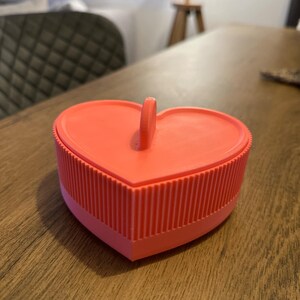 May include: A bright pink heart-shaped trinket box with a ribbed texture and a small handle on top.
