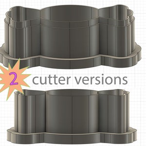 May include: Two versions of a cookie cutter in the shape of a bow tie. The cutter is made of a dark gray plastic.