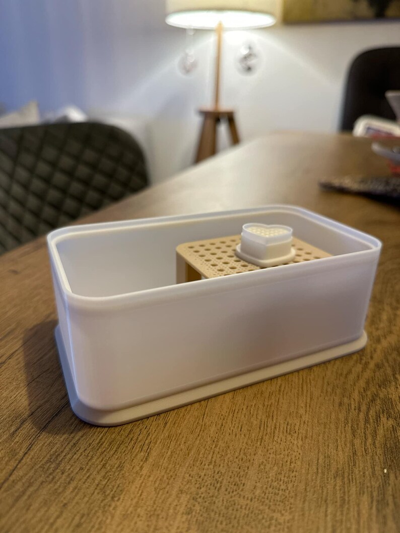 May include: A white plastic container with a beige insert and a white heart-shaped lid. The container is designed for storing small items.