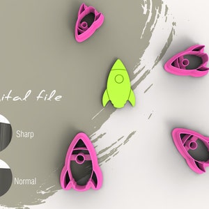 May include: Five rocket-shaped cookie cutters, four are pink and one is green. The cookie cutters are on a light brown background with a white brushstroke design. The text "Digital file" is written in black on the background.