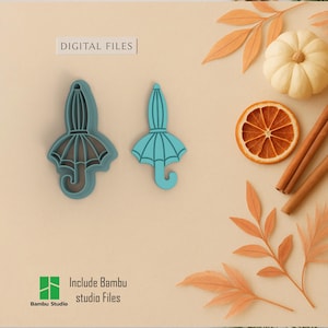 Puede incluir: Dos cortadores de galletas en forma de paraguas de color turquesa. La imagen incluye el texto "DIGITAL FILES" y "Include Bambu studio Files". Los cortadores están junto a una pequeña calabaza blanca, una rodaja de naranja seca y palitos de canela.