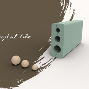 Puede incluir: Un bloque verde claro con tres agujeros redondos y un borde dentado. El bloque está sobre una superficie blanca. Hay tres esferas beige sobre una superficie marrón con pinceladas blancas.