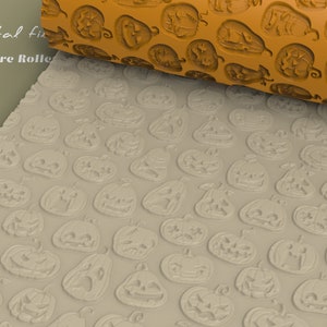 Può includere: Primo piano di un mattarello beige con un motivo ripetuto di facce di zucca. Il mattarello viene utilizzato per creare un'impronta del motivo di zucca su una superficie beige. Il testo "Digital fix Texture Roller" è visibile nell'angolo in alto a sinistra dell'immagine.