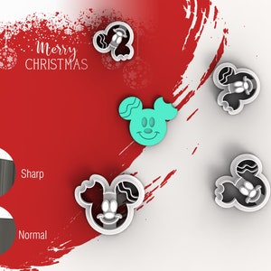 May include: Four cookie cutters in the shape of Mickey Mouse's head. The cutters are silver and have a black outline. One cutter is teal blue and has a smiling face. The text "Merry Christmas" is in the background.