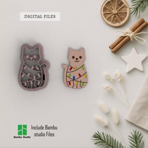 May include: Two cat-shaped cookie cutters, one a mold and the other a finished product, both decorated with Christmas lights. The finished cat is tan with colourful lights. The mold is a darker shade of tan. The words "DIGITAL FILES" are at the top.