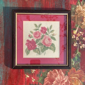 Può includere: Opera d'arte a punto croce incorniciata con un bouquet di rose rosa e rosse con foglie verdi. L'opera è incorniciata in una cornice di legno scuro con un bordo interno dorato e un passe-partout rosa. Forma quadrata.
