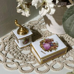 May include: Two small, white porcelain boxes with gold trim and lids featuring a couple in period dress. One box is a small grinder with a gold handle. The other box is rectangular and has the word "Limoges" on it.