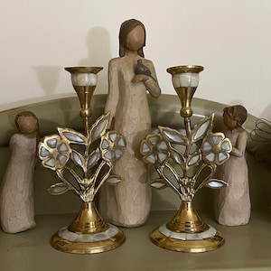 Peut inclure: Deux bougeoirs dorés avec des motifs floraux et des accents blancs. Les bougeoirs sont sur une étagère avec plusieurs figurines en bois en arrière-plan. Les bougeoirs ont une base décorative.
