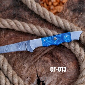 May include: A Damascus steel knife with a blue and silver handle. The handle has a marbled blue pattern and is accented with silver bolsters. The blade has a unique pattern. The text "CF-013" is visible.