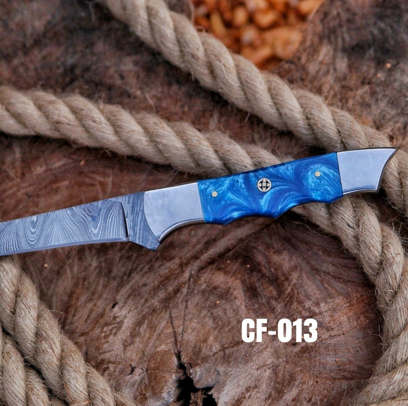 May include: A Damascus steel knife with a blue and silver handle. The handle has a marbled blue pattern and is accented with silver bolsters. The blade has a unique pattern. The text "CF-013" is visible.