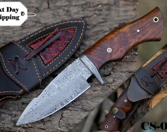 May include: A Damascus steel knife with a wooden handle and a leather sheath. The handle is a rich brown color with decorative rivets. The sheath is black with red accents and a stitched design. The knife is labeled "CS-011".