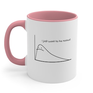 May include: White ceramic mug with a pink interior and handle. The mug features a black line drawing of a curve with a sad face and the text "I just want to be normal."