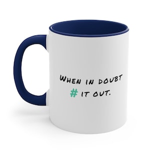 May include: White ceramic coffee mug with a navy blue rim and handle. The mug has a black handwritten message that reads "WHEN IN DOUBT # IT OUT."