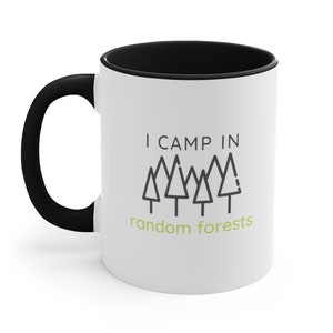 May include: White ceramic mug with a black rim and handle. The mug has a black and green design with the text "I CAMP IN random forests" and a row of five stylized trees.