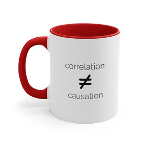 May include: White ceramic mug with a red rim and handle. The mug has black text that reads "correlation does not equal causation".