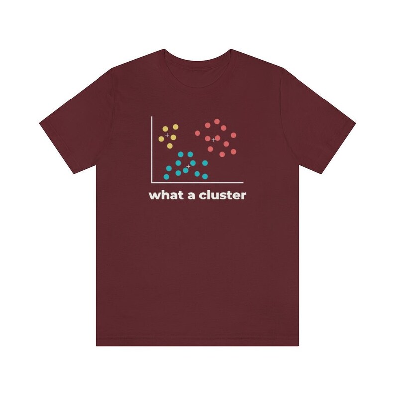 May include: Maroon t-shirt featuring a data visualization graphic with yellow, red, and blue dots, and the text "what a cluster" in white. The graphic resembles a scatter plot, with dots grouped together. The shirt is made of a soft material.