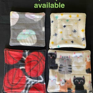 May include: Four different fleece squares with various designs. The squares are red with black basketballs, grey with pastel cupcakes, white with blue stars, and beige with cats.