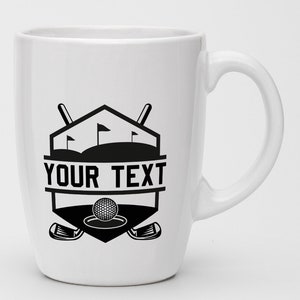 May include: White ceramic coffee mug with a black and white golf-themed design. The design features a golf ball, golf clubs, and a golf course with flags. The text "YOUR TEXT" is printed on the mug.
