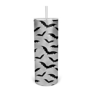 May include: A silver tumbler with a black bat pattern. The tumbler has a clear lid and a clear straw.