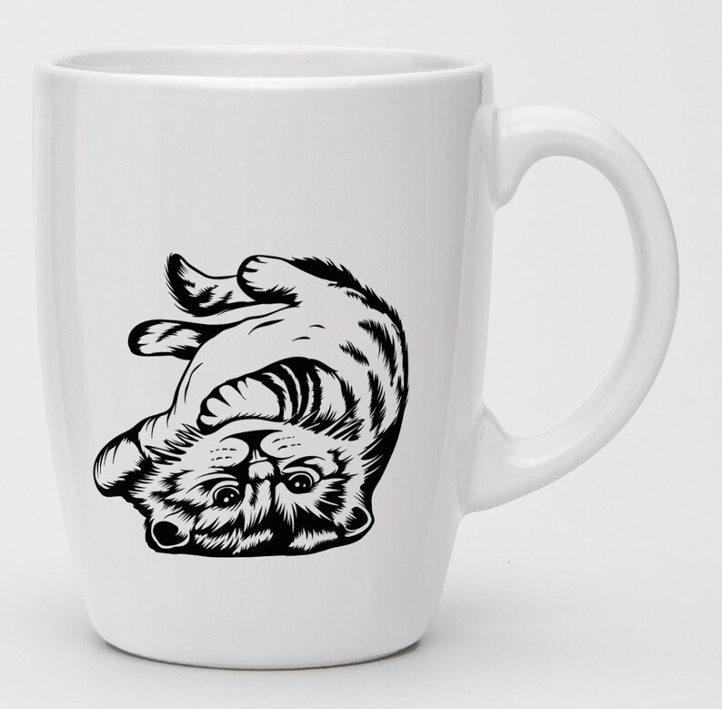 May include: White ceramic mug with a black and white illustration of a cat upside down. The cat is looking up with its paws in the air.