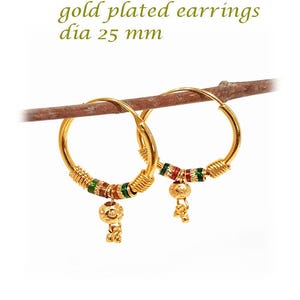 May include: Gold plated hoop earrings, 25 mm in diameter, with colourful accents. The earrings have a small dangling charm. The text "gold plated earrings dia 25 mm" is visible in the image.