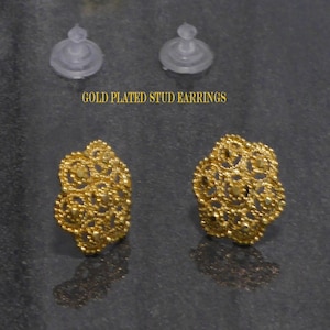 May include: A pair of gold-plated stud earrings with a delicate, intricate design. The earrings are small and round, with a filigree pattern.