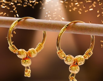May include: A pair of gold hoop earrings featuring a textured finish. Each earring has a circular band adorned with three small, spherical beads at the base, accented by coiled wire details on the sides and small dangling elements at the bottom.