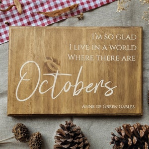 Peut inclure: Une pancarte en bois avec une teinte brune et des lettres blanches. La pancarte indique "I'M SO GLAD I LIVE IN A WORLD WHERE THERE ARE Octobers ANNE OF GREEN GABLES".