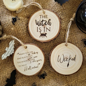 Peut inclure: Trois ornements ronds en bois avec des dictons sur le thème d'Halloween. Le premier ornement dit "The Witch Is In" avec une silhouette de chat noir. Le deuxième ornement dit "When Witches Go Riding And Black Cats Are Seen The Moon Laughs & Whispers Tis Near Halloween". Le troisième ornement dit "Wicked".