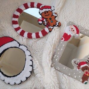 May include: Three Christmas-themed mirrors with white, red, and gray yarn embroidery. The mirrors are shaped like a candy cane, a Santa hat, and a snowflake. The candy cane mirror features a gingerbread man, the Santa hat mirror features a Santa Claus, and the snowflake mirror features a reindeer.