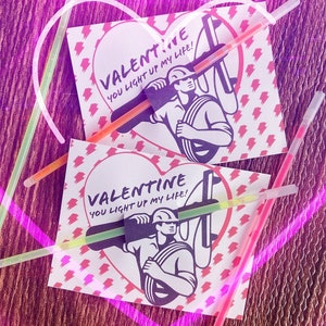 May include: Two Valentine's Day cards with a heart shape and a cartoon electrician holding a wire. The text on the cards reads "Valentine You Light Up My Life!"