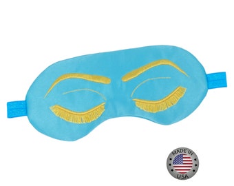 May include: A light blue sleep mask with embroidered eyelashes and eyebrows. The mask is made in the USA.