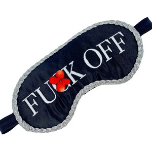 Puede incluir: Máscara de dormir negra con ribete plateado y la frase "F**K OFF" bordada en blanco. Una flor roja está bordada en la máscara.
