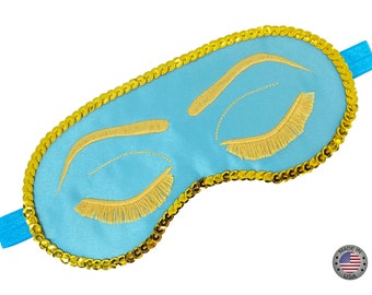 May include: A light blue sleep mask with gold sequins around the edges and embroidered eyelashes. Made in the USA.