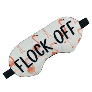 May include: A white sleep mask with a black elastic strap. The mask is decorated with pink flamingos and the text "Flock Off" in black embroidery.