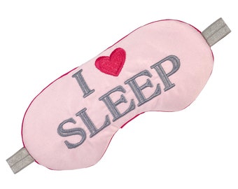 Può includere: Una mascherina per dormire rosa con la scritta ricamata "I LOVE SLEEP" in grigio. Un cuore rosso è ricamato sopra la parola "SLEEP". La mascherina ha un elastico grigio e un bordo rosso.
