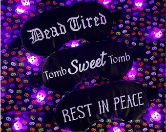May include: Three black sleep masks with white text. The first mask says "Dead Tired", the second says "Tomb Sweet Tomb", and the third says "Rest In Peace".