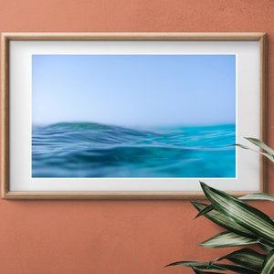 May include: A framed photograph of a blue ocean wave with a light blue sky in the background.
