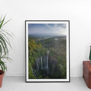 Può includere: Una vista aerea di una cascata che scende da una scogliera verde e lussureggiante. La cascata è circondata da una vegetazione fitta e nebbia, creando una scena serena e pittoresca.