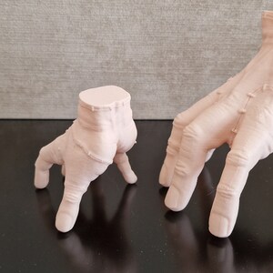 Op de afbeelding: Drie verschillende maten, lichtroze, 3D-geprinte handen met elk vier vingers. De handen zijn geposeerd alsof ze op handen en voeten lopen.